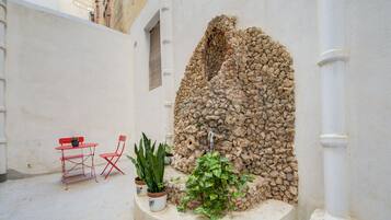 Une cour avec un mur en pierre, une petite table avec une chaise et des plantes en pot.