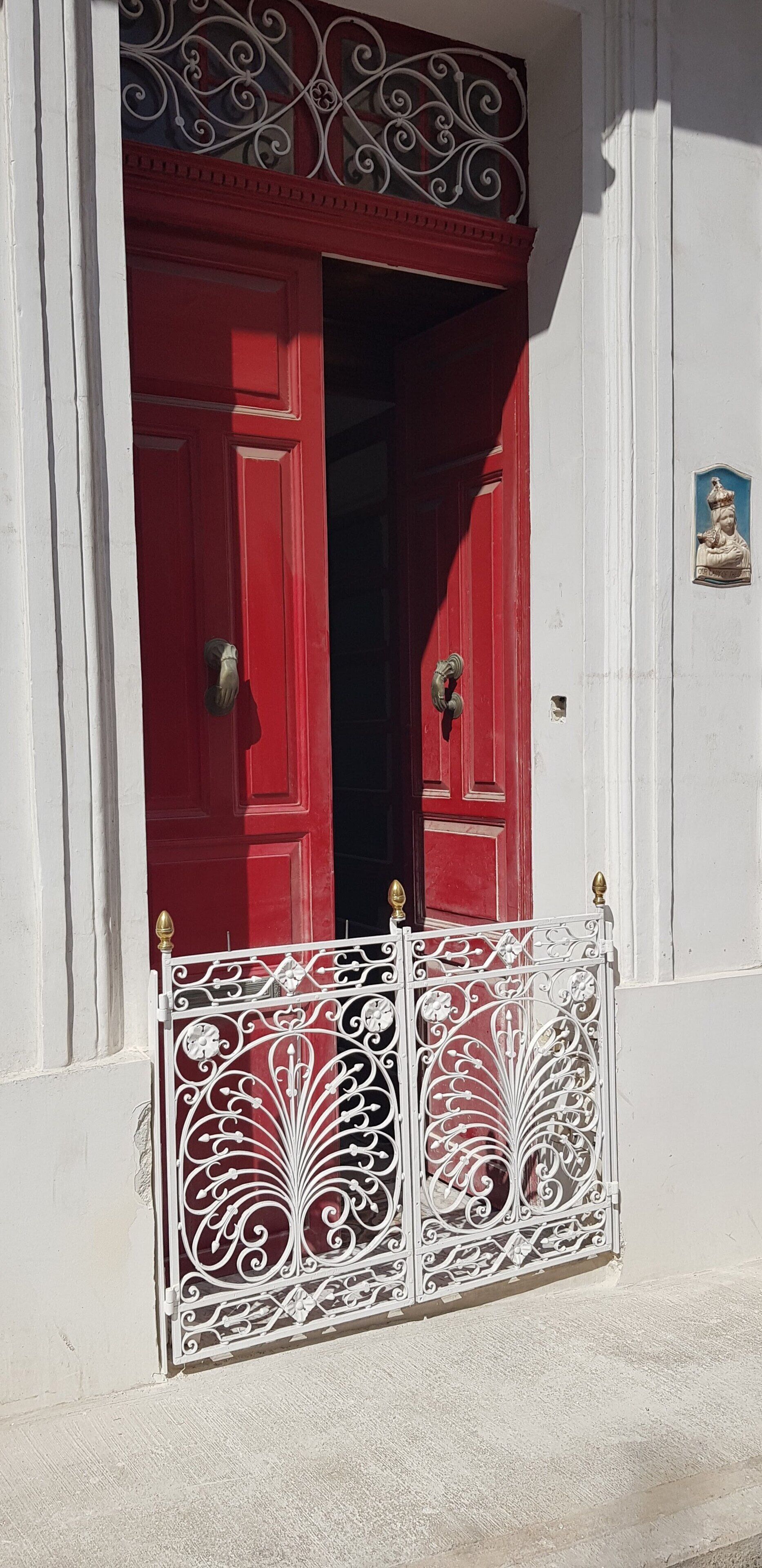 Une porte rouge ornée de motifs métalliques, un mur blanc et une petite plaque.