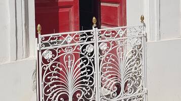 Une porte rouge ornée de motifs métalliques, un mur blanc et une petite plaque.