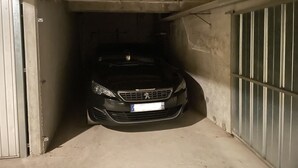 A car parked in a narrow, dimly lit parking garage with concrete walls and metal gates.