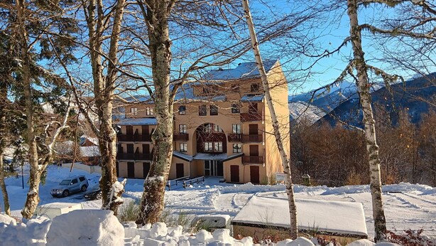 A multi-story building with a central courtyard, surrounded by snow-covered trees and mountains in the background.