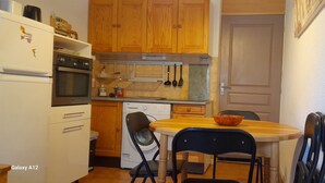 A compact kitchen with wooden cabinets, a built-in oven, a washing machine, and a dining area with a table and chairs.