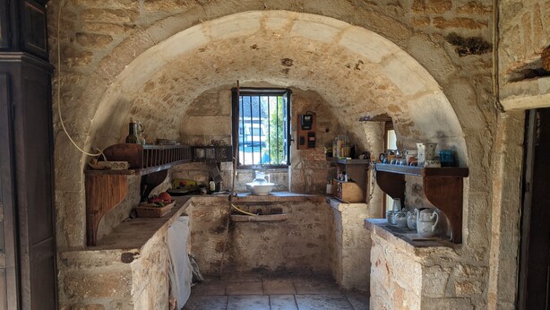 A narrow stone-walled corridor with a window at the end, leading to a room with a stone floor and various kitchen items on shelves. - Le Domaine de Magnagues (Carennac)