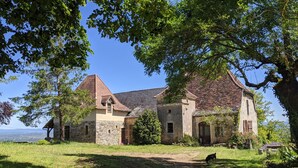 A stone building with a tiled roof, surrounded by lush greenery and a clear view of the sky. - Le Domaine de Magnagues (Carennac)
