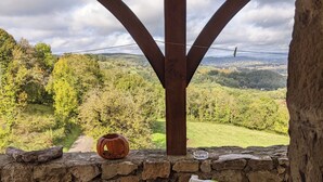 A stone wall with a rustic table and chairs, a pumpkin, and a view of a green landscape under a wooden structure. - Le Domaine de Magnagues (Carennac)