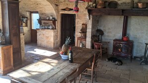 A rustic kitchen with stone walls, wooden furniture, a wooden table, a red hanging lamp, a dog, and a vintage stove. - Le Domaine de Magnagues (Carennac)