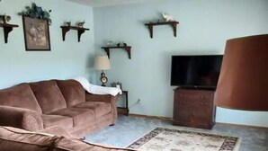 A living room with a brown sofa, a television, and wall-mounted shelves. - Blue Elephant Cottage (Sullivan)