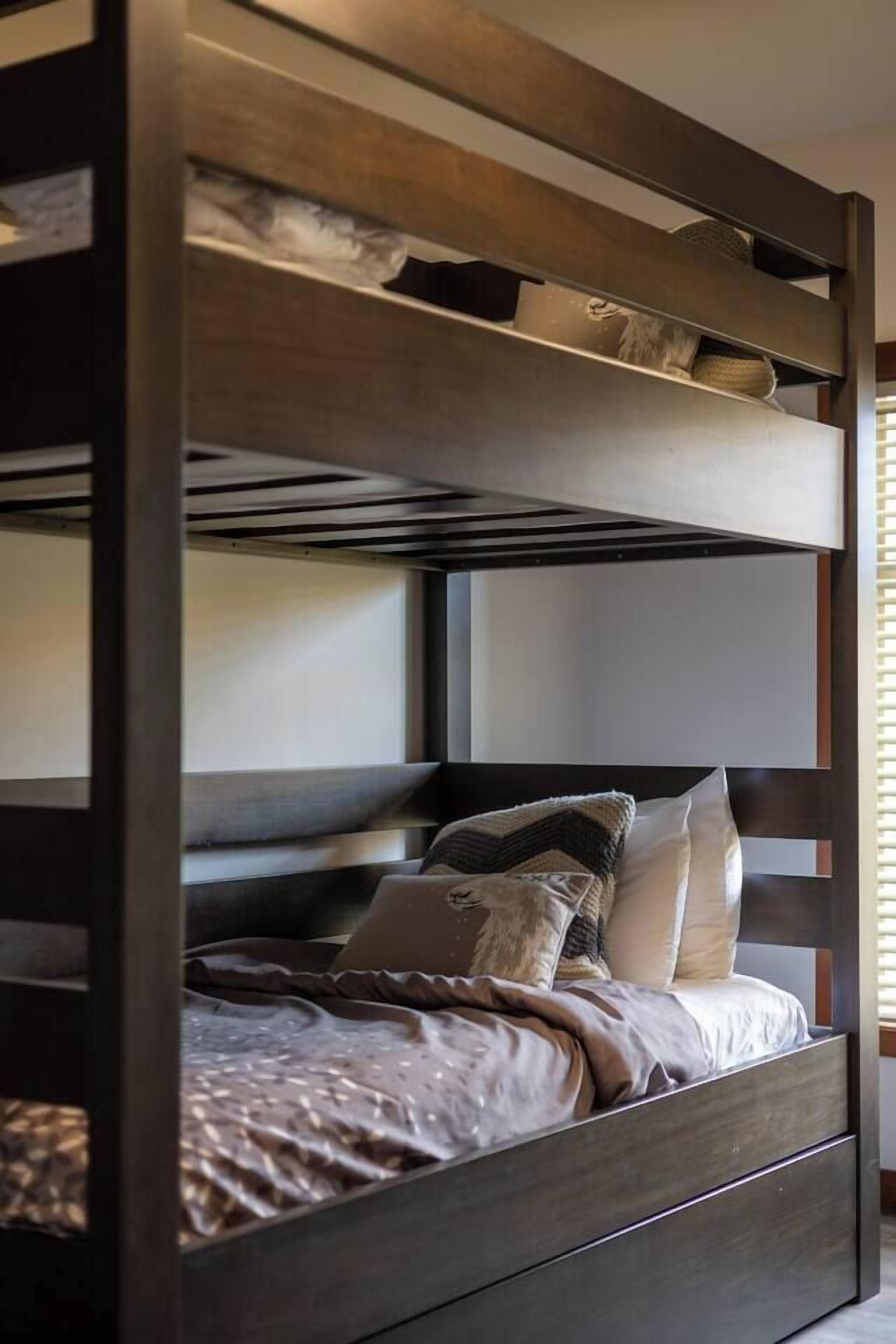 A bunk bed with a wooden frame, a lower bed with a patterned blanket, and pillows.