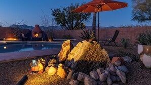 Un área de piscina con un jardín rocoso, una chimenea y una sombrilla.