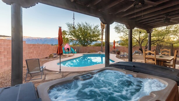 Un jacuzzi con vistas a montañas, piscina y mobiliario exterior.