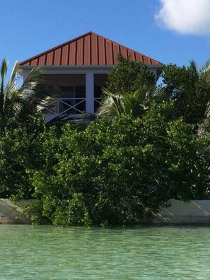 A building with a red roof and white walls, surrounded by dense greenery and a body of water.
