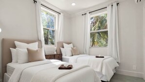 Habitación de hotel con dos camas, un ventilador de techo y ventanas grandes con cortinas.