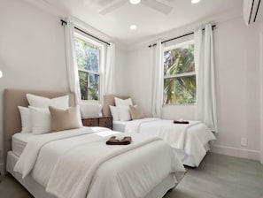 Habitación de hotel con dos camas, un ventilador de techo y ventanas grandes con cortinas.