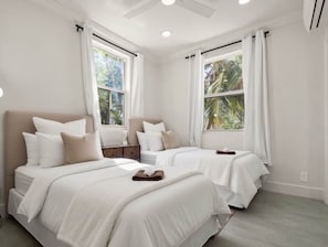 A hotel room with two beds, a ceiling fan, and large windows with curtains.