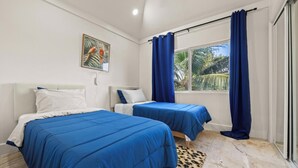 A bedroom with two beds, a window with curtains, a painting on the wall, and a patterned rug. - Lo key cottages estate (Green turtle cay)