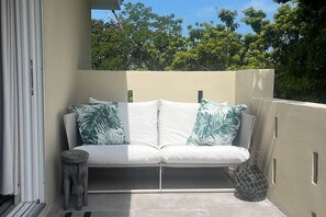 A balcony with a white sofa, two pillows with a leaf pattern, a small stool, and a woven basket. - 2 Apartments , 1 home , sleeps 16 on Coco Bay (Green turtle cay)