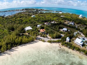 An aerial view of a coastal property with multiple buildings, clear turquoise waters, and a sandy beach.