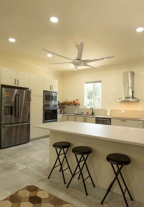 A modern kitchen with stainless steel appliances, a central island with stools, and recessed ceiling lighting. - Lo key cottages estate (Green turtle cay)