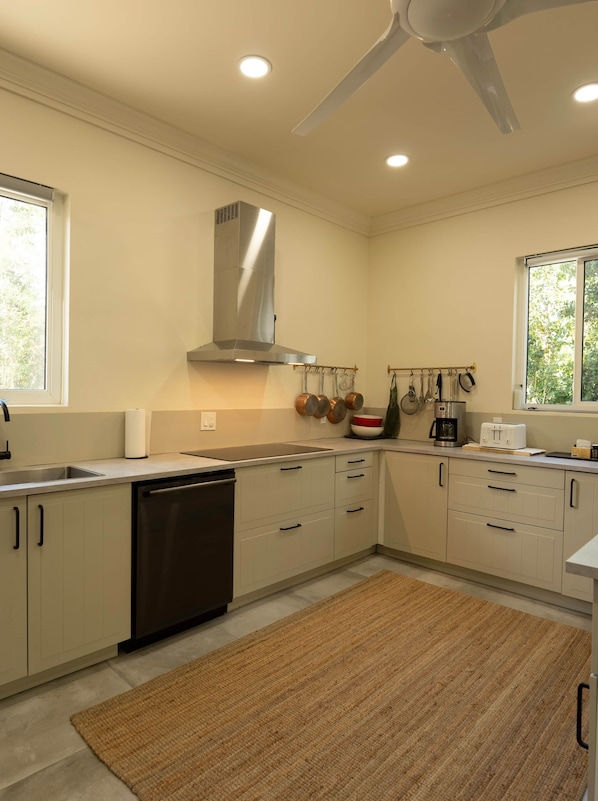 A modern kitchen with a dishwasher, a stainless steel range hood, and a hanging pot rack.