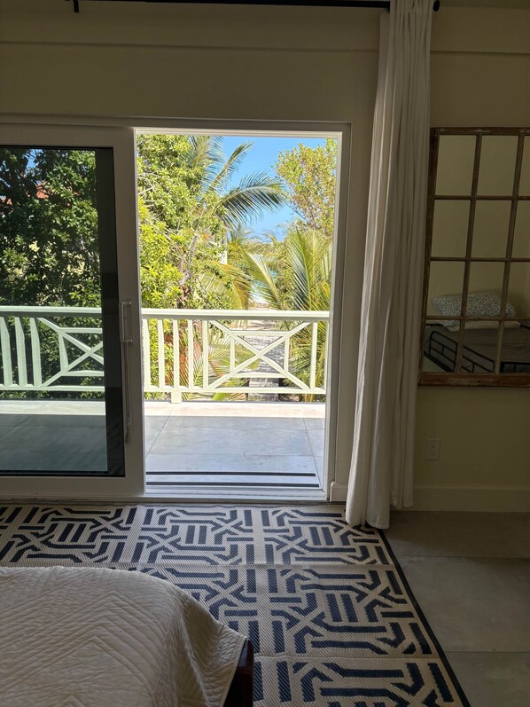 A room with a bed, a patterned rug, a view of a balcony with a railing, and a window with a curtain. - Lo key cottages estate (Green turtle cay)