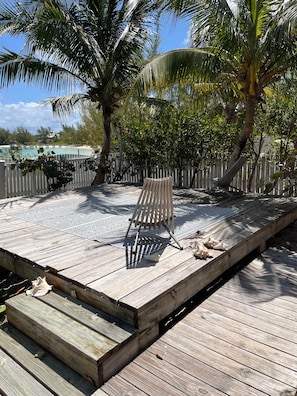 A wooden deck with a metal chair, surrounded by palm trees and a white fence.
