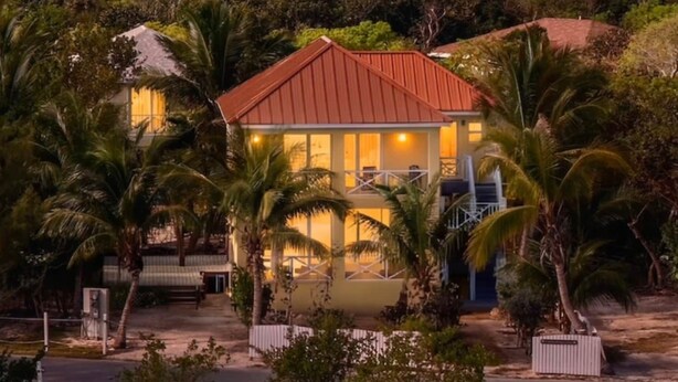 Una propiedad frente a la playa con una casa destacada de techo rojo, rodeada de exuberante vegetación y palmeras.