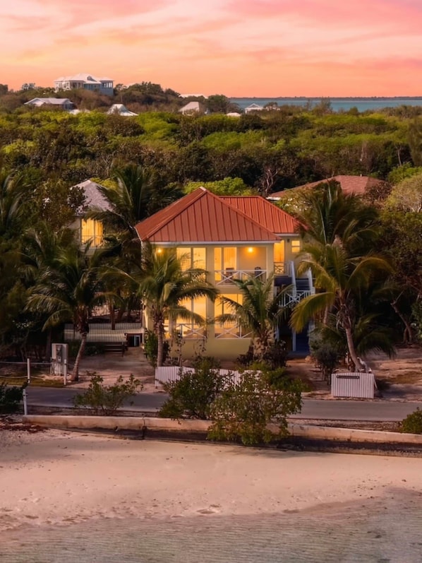 Una propiedad frente a la playa con una casa destacada de techo rojo, rodeada de exuberante vegetación y palmeras.