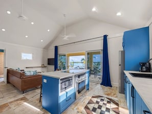 A modern kitchen with a central island, a dining area with a brown sofa, and a view of a pool through a sliding glass door.
