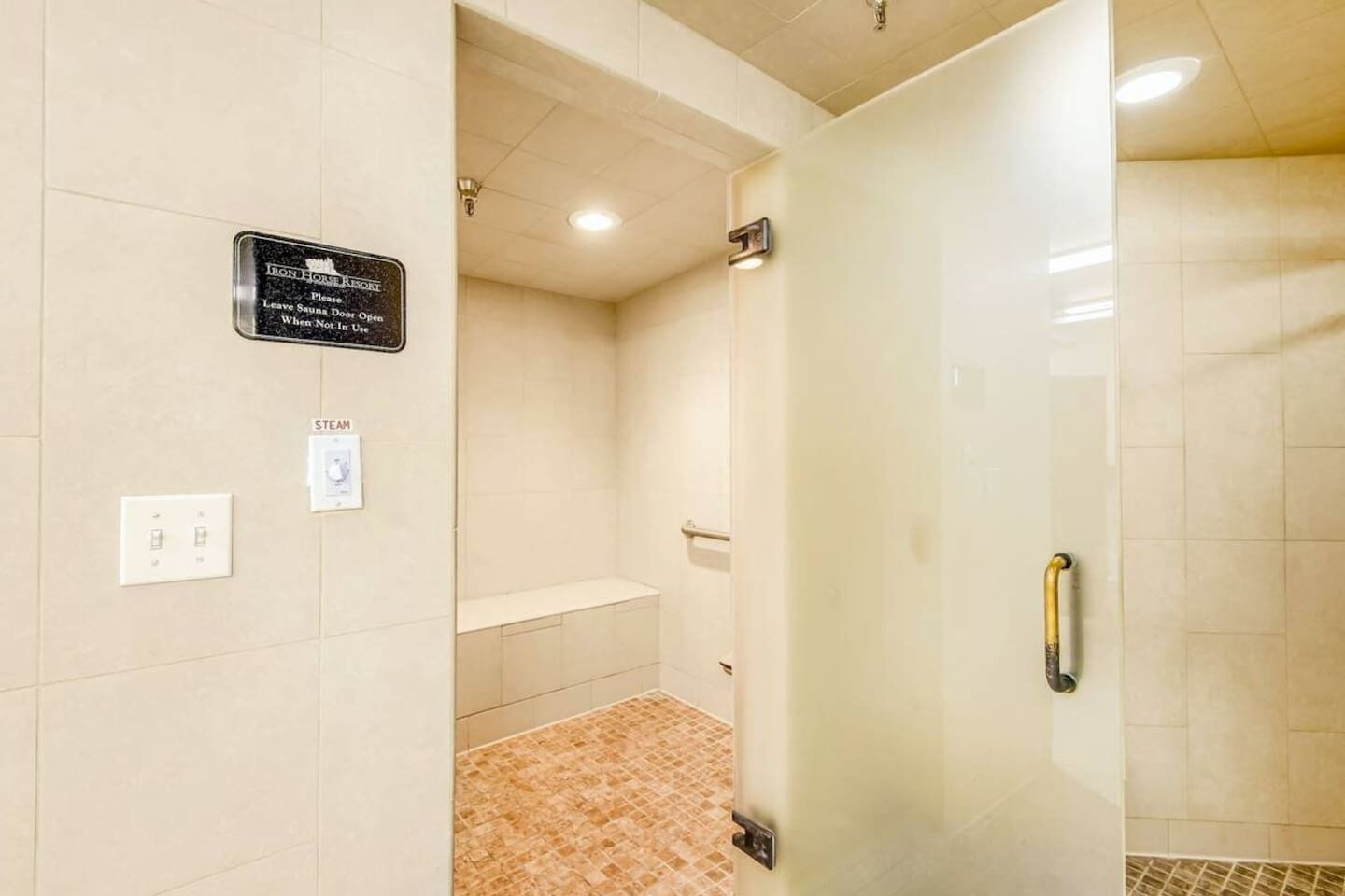 A hotel bathroom with a glass shower door, a sign indicating the sauna is not in use, and a steam feature.
