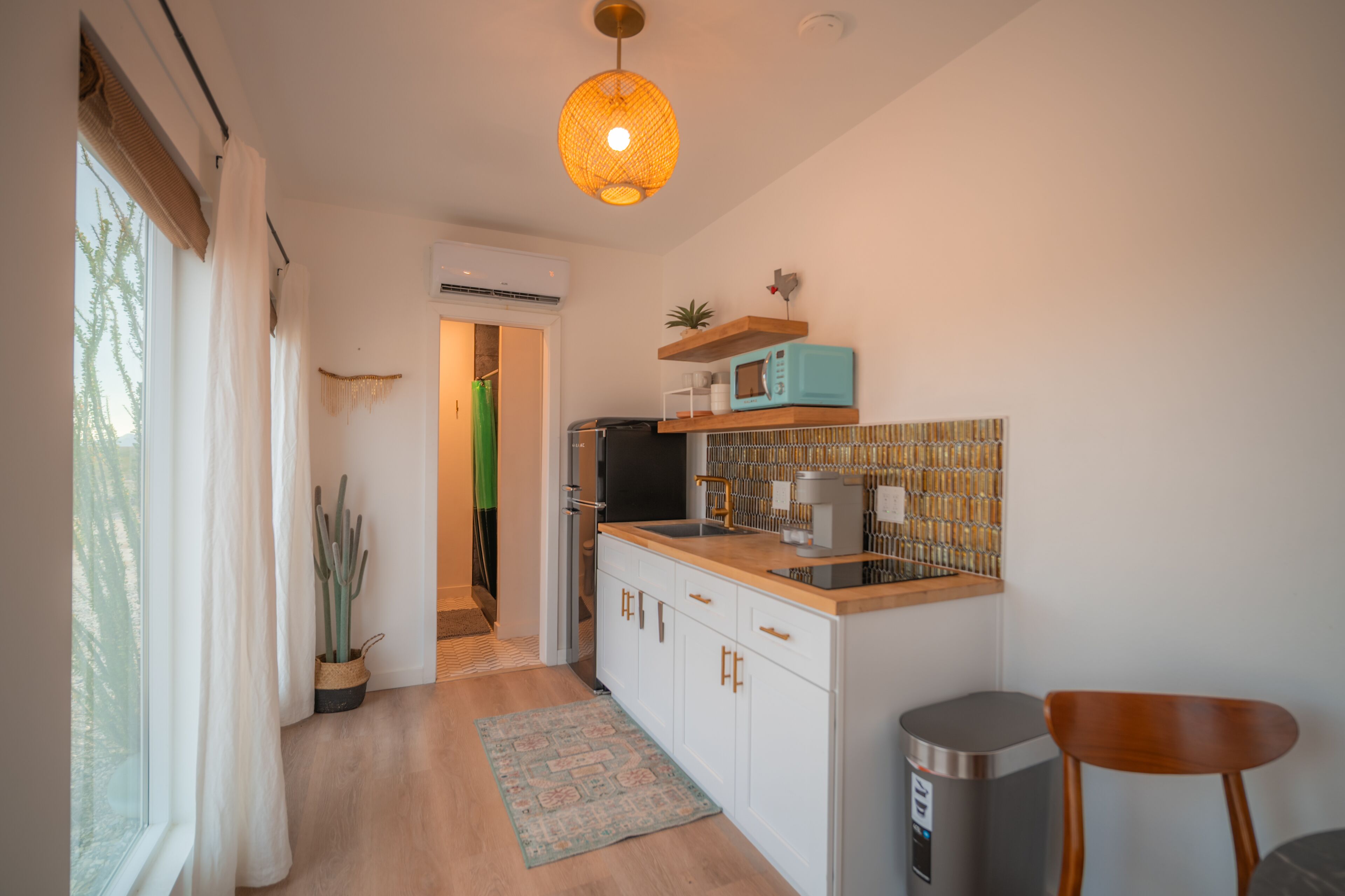 Eine kleine Küche mit weißen Schränken, einer Holzausziehtafel, einer Mikrowelle und einer Pendelleuchte.