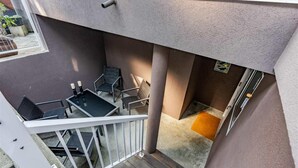 Ein Balkon mit Glastisch und Stühlen, einem kleinen Fenster und einer Tür mit Fußmatte.