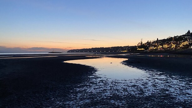 Ein Strand im Dämmerlicht, das ruhige Wasser spiegelt den Himmel wider.