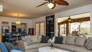 Un salon spacieux avec un canapé, une table basse et des fauteuils. Il y a également un coin repas avec une table et des chaises. Une pancarte indique : « L’Oasis ».