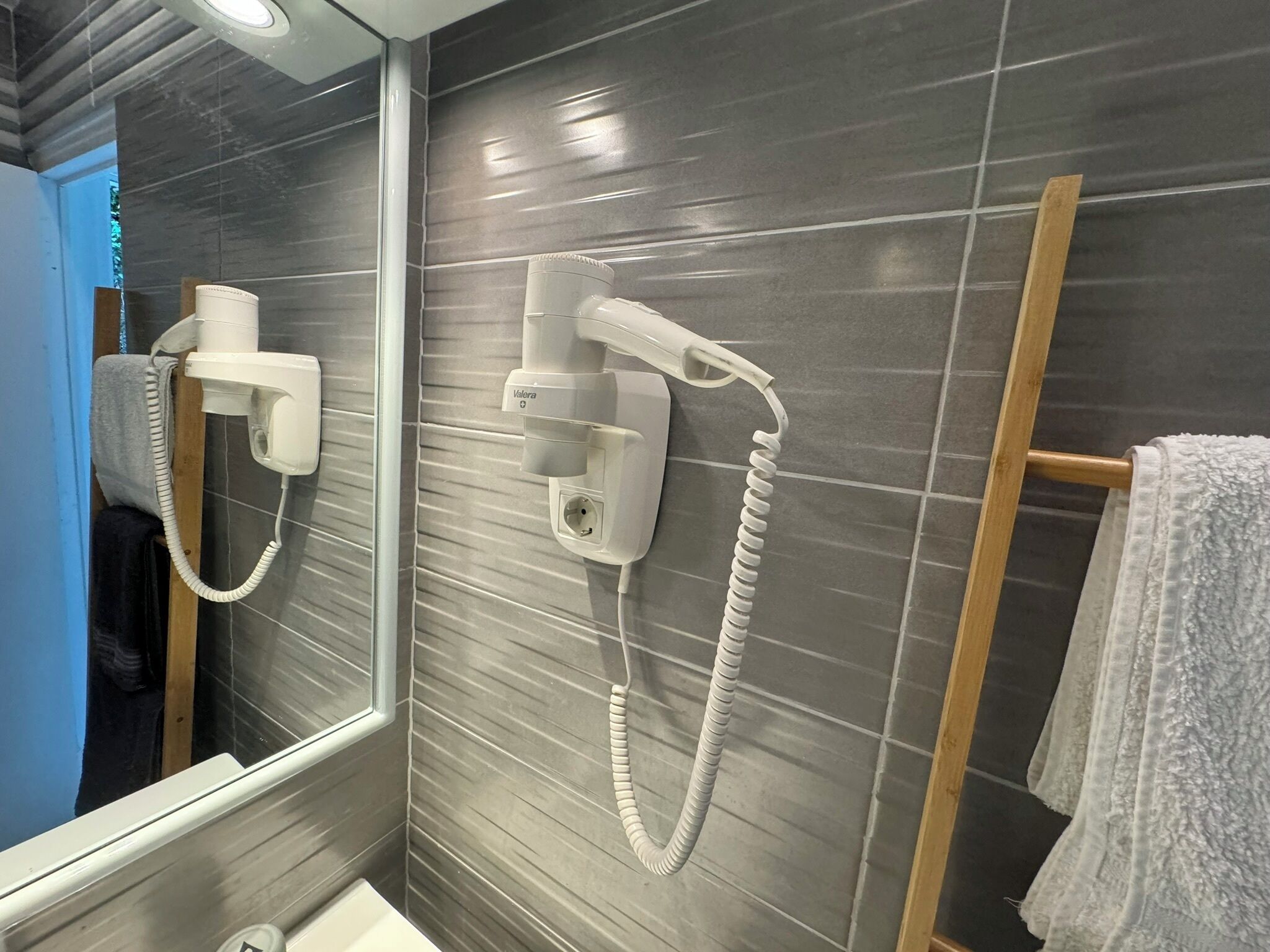 Ein Badezimmer mit Spiegel, zwei an der Wand befestigten Haartrocknern und einem Handtuchhalter mit einem weißen Handtuch.
