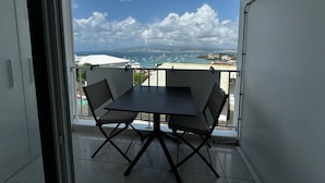 A balcony with a table and chairs, offering a view of the sea and boats. - Studio Voilier - Résidence de la Baie Anse-mitan (Les Trois-Îlets)