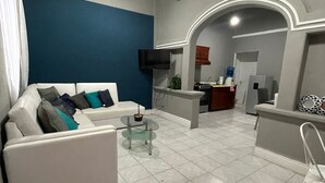 A living room with a white sofa, a glass coffee table, and a TV mounted on the wall.