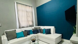 A living room with a white sofa, a glass coffee table, and a blue accent wall.