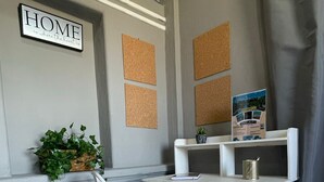 A corner room with a white chair, a small white table with baskets, a corkboard wall, and a 'HOME is where the heart is' sign.