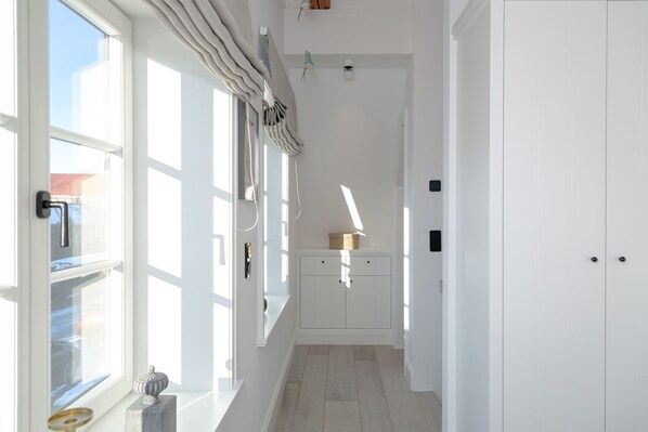 A bright hallway with white walls, a wooden floor, and a door at the end.