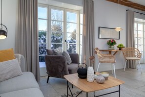 Una sala moderna con un sofá gris, un sillón oscuro, una mesa de centro de madera y un comedor con sillas de mimbre.