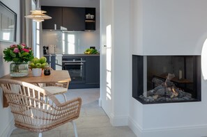 Una cocina moderna con armarios oscuros, un comedor con sillas de mimbre y una chimenea.