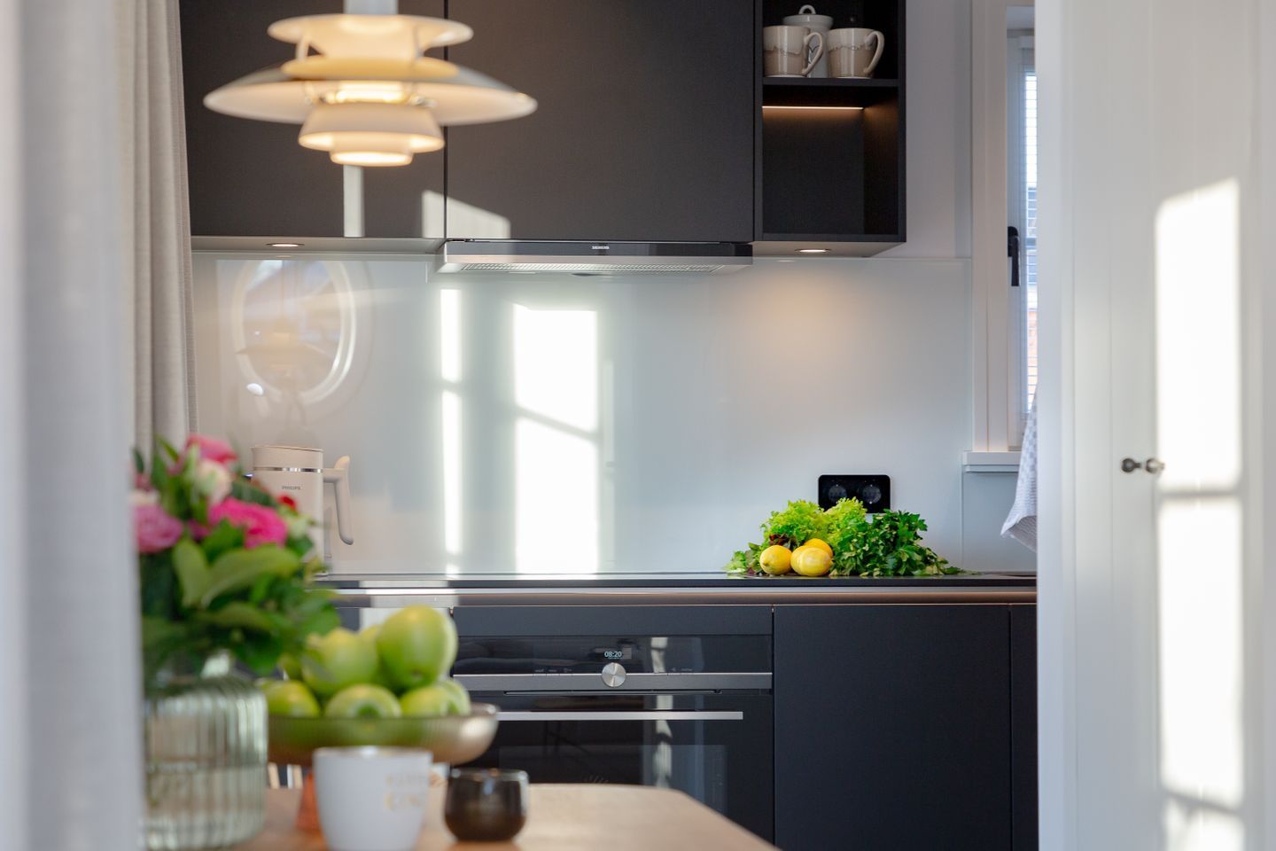 A modern kitchen with a stainless steel range hood, a black cabinet, and a small window.