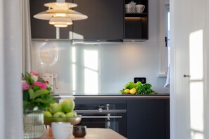 A modern kitchen with a stainless steel range hood, a black cabinet, and a small window. - NEU 2023 - Sylter Meerwind - NEU 2023 - Helle Zwei Zimmer Wohnung im Herzen von Alt Westerland (Sylt)