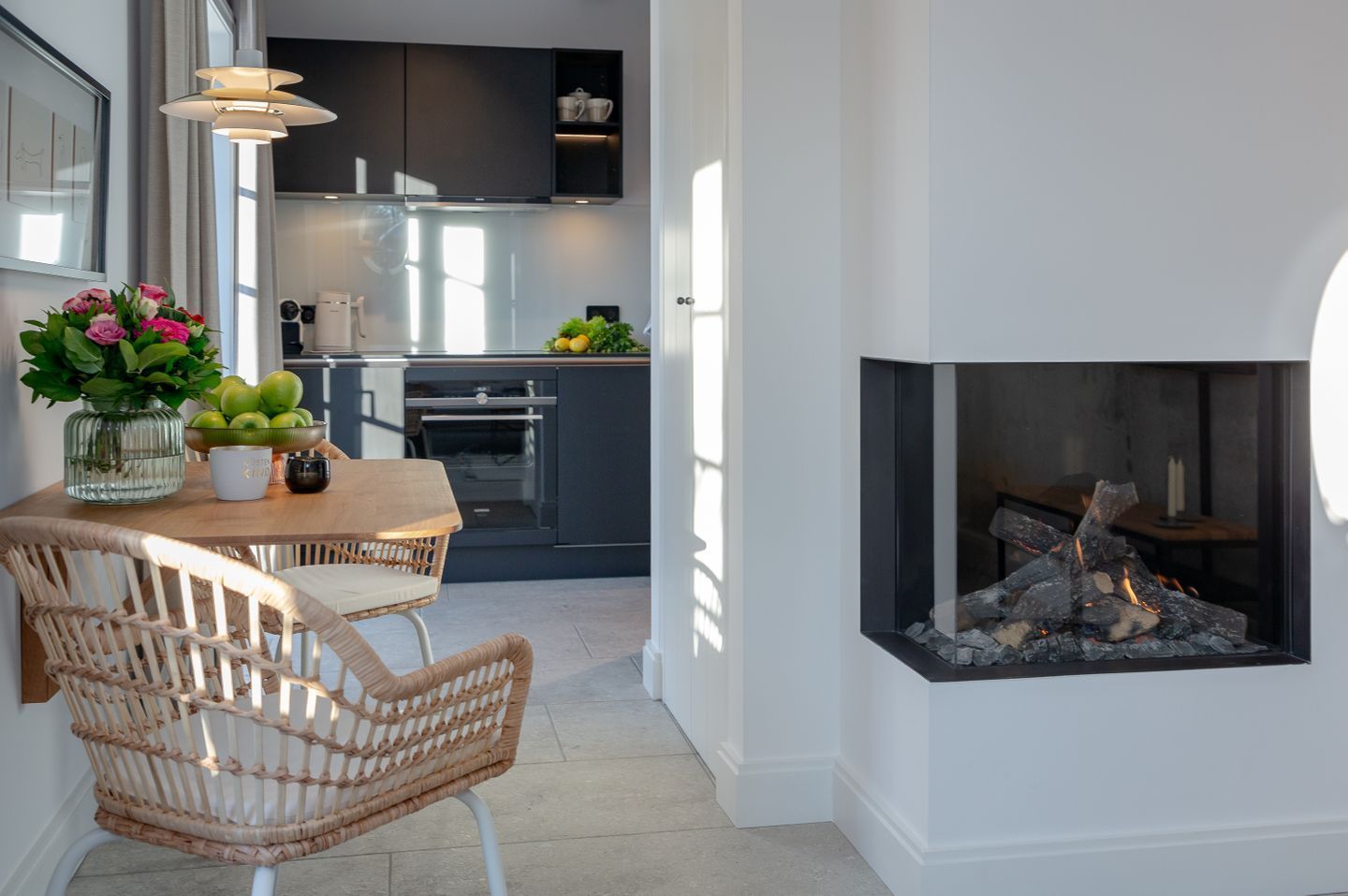 A modern kitchen with dark cabinets, a dining area with wicker chairs, and a fireplace.