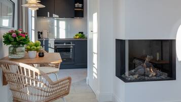 A modern kitchen with dark cabinets, a dining area with wicker chairs, and a fireplace.