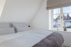 Un dormitorio con una cama grande, una ventana que da a un edificio y una lámpara en la mesita de noche.