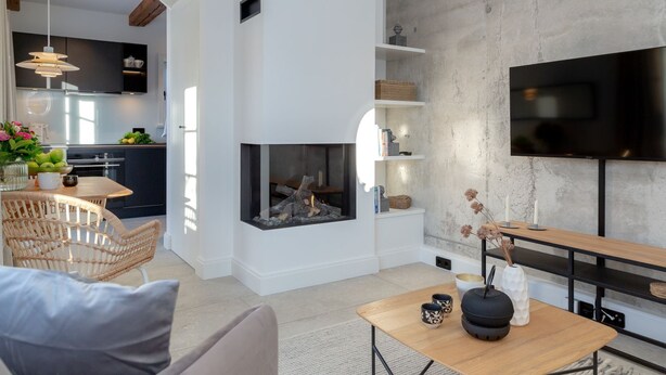 A modern living room with a fireplace, a dining area, and a kitchen in the background. - NEU 2023 - Sylter Meerwind - NEU 2023 - Helle Zwei Zimmer Wohnung im Herzen von Alt Westerland (Sylt)