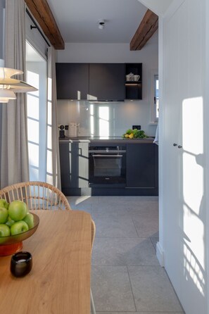 Una cocina moderna con armarios oscuros, una mesa de comedor de madera con un tazón de manzanas verdes y una taza negra pequeña.