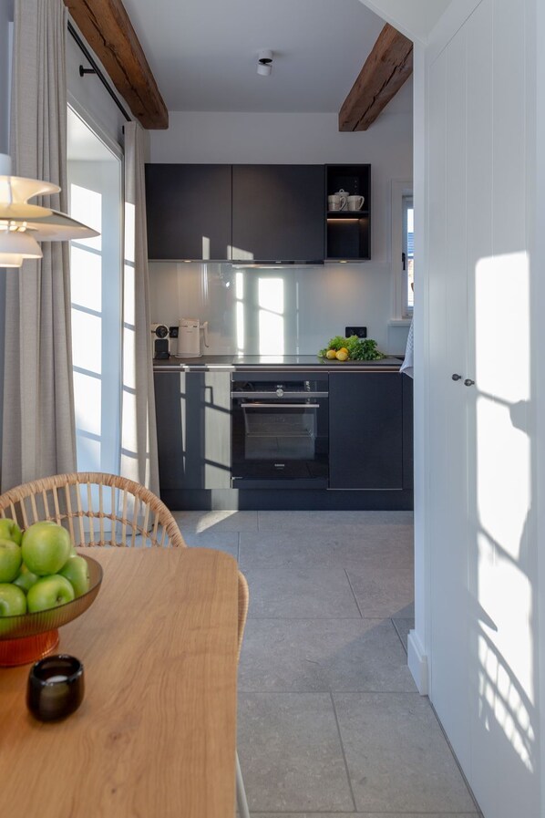 Una cocina moderna con armarios oscuros, una mesa de comedor de madera con un tazón de manzanas verdes y una taza negra pequeña.