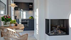 A modern kitchen with dark cabinets, a dining area with wicker chairs, and a fireplace. - NEU 2023 - Sylter Meerwind - NEU 2023 - Helle Zwei Zimmer Wohnung im Herzen von Alt Westerland (Sylt)